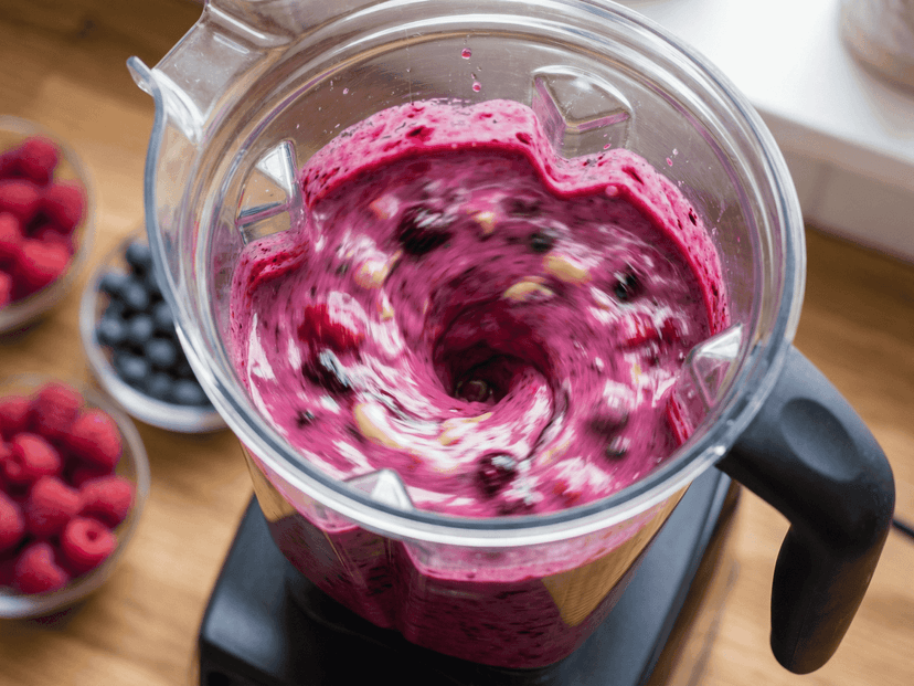 Blender z różową masą jagodową otoczony malinami i borówkami — proces tworzenia deseru bez cukru